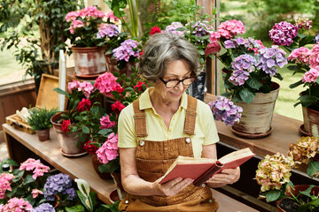 Beautiful senior woman enjoys reading in a vibrant garden filled with blooming flowers