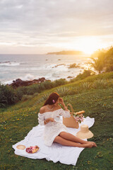 Elegant Woman Enjoying Sunset Picnic By The Ocean With Tea And Flowers 