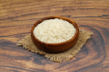 Raw white rice on black background. Long uncooked rice in wooden plate. Natural organic food. Traditional Asian cereal culture.