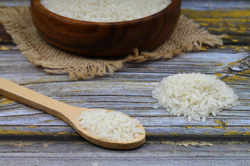 Raw white rice on black background. Long uncooked rice in wooden plate. Natural organic food. Traditional Asian cereal culture.