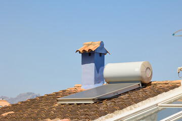 Close-up view of a solar water heater system mounted on a traditional clay-tiled rooftop next to a...