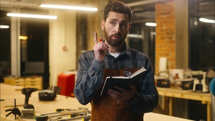 Contemplative Caucasian guy thinking writing notebook in workshop male wood master joiner carpenter...