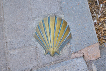 Close-up of a bronze scallop shell embedded in a sidewalk, marking the Camino de Santiago...
