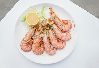 Grilled prawns with sliced fried garlic and half a lemon served on a white plate at a traditional Spanish coastal tapas restaurant