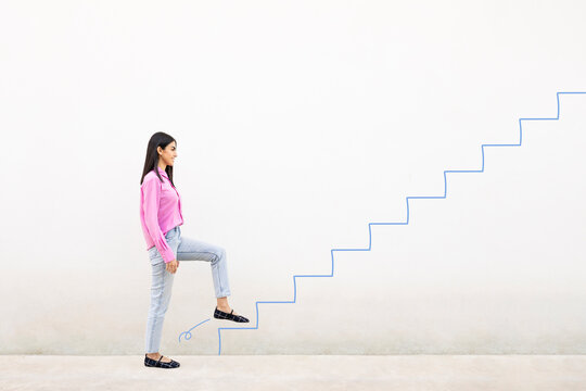 Young woman in pink shirt smiling and climbing illustrated stairs on a white wall