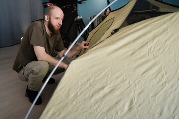 Preparing for a hike in the mountains. Packing a tent for camping at home. Bearded man hiker...