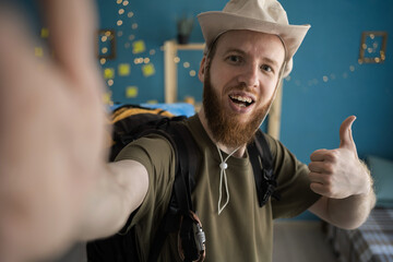 Handsome bearded man taking selfie on smartphone at home indoors Traveler guy looking at camera...
