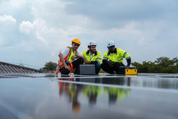 Group of solar engineers in safety gear discussing installation plans on rooftop, using laptop and...