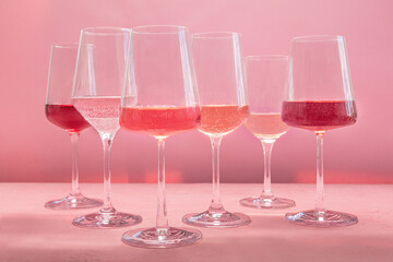 Rose wine, a variety of hues and tints, side view on a pink background, many wineglasses, summer party