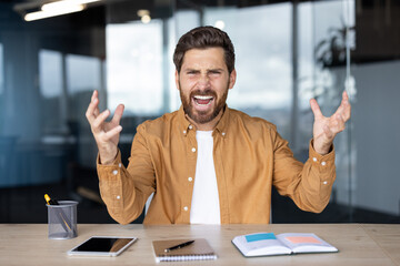 A frustrated man in a professional setting, expressing anger and exasperation, gesturing with his...
