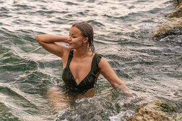 Fototapeta premium Woman Swimsuit Ocean - A woman in a black swimsuit sits in the ocean waves.