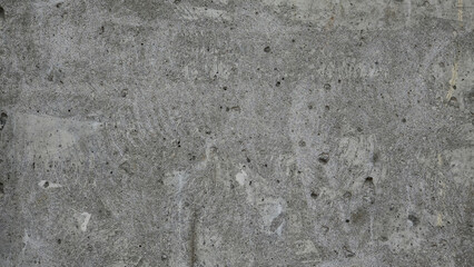 A grey concrete wall with a lot of small rocks on it. The wall is very rough and has a lot of...