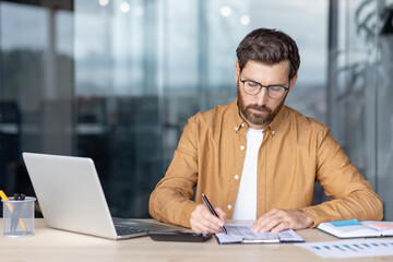 A focused businessman in glasses reviews documents at his desk, highlighting a concept of financial analysis.