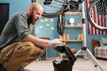 Caucasian bearded man opening toolbox with tools repairing bicycle at home. Bike maintenance
