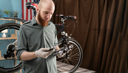 Bearded man repairing bicycle indoors, choosing proper wrenches from toolset for bike maintenance....