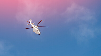 A white helicopter is flying in the sky. The sky is blue and the clouds are white. The helicopter...