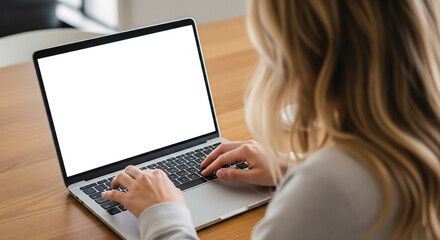 Rear view of a woman working on a laptop computer at a wooden table.