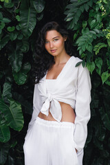 Elegant Woman in White Crop Top Posing in Front of Lush Green Foliage