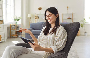 Happy woman uses tablet pc for communication during online video call and conversation at home,...