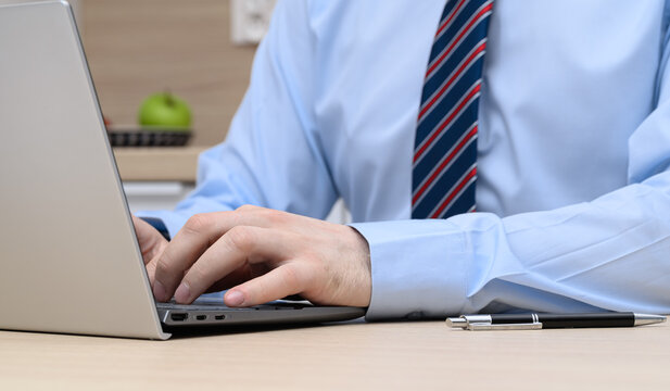 Close-up of a smartly dressed man typing on a laptop keyboard