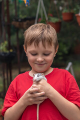 Boy holds pet rat in his hands outside and smiles