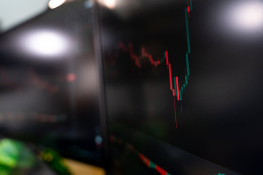 Close-up candlestick stock chart on monitor in modern studio setup with triple displays, perfect for visuals about trading, cryptocurrency, or financial analysis environments.