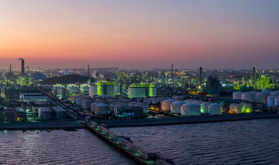 Aerial view of a large coastal oil refinery and petrochemical plant with illuminated storage tanks at dusk