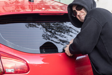 A hooligan man commits illegal actions with someone else's car. He is trying to break off the rear wipers on the car.