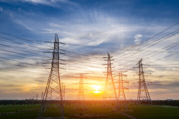 High voltage power tower and transmission lines silhouetted against beautiful sunset sky in a rural field