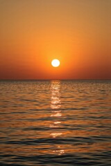 Obraz premium Colorful sunset sky glowing above gentle waves on sandy beach shoreline, perfect for coastal travel visuals and wellness imagery