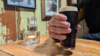 A hand holding a glass of dark fresh beer in a traditional vintage irish pub. copy space