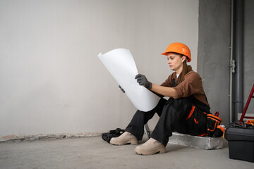 female contractor reading blueprint sitting floor before home renovation