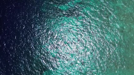 Aerial top-down view of boats over deep blue and emerald waters with circular patterns. Sunny day highlights the vibrant sea texture.