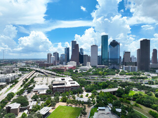 A stunning aerial drone photography of downtown Houston, Texas, showcasing the city's iconic skyline under a vibrant blue sky filled with dramatic cumulus clouds. Prominent high-rise buildings © Visual Art Complex
