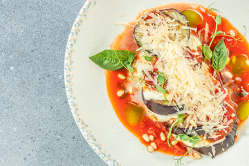 A gourmet serving of eggplant parmesan is elegantly plated with rich tomato sauce, melted cheese, fresh basil, pine nuts, and a generous topping of grated parmesan