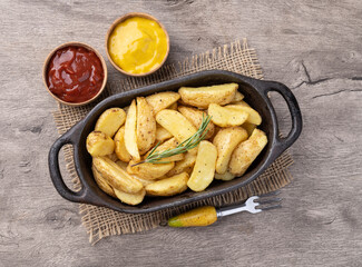 Rustic baked potatoes in a plate with ketchup, mustard and beer over wooden table