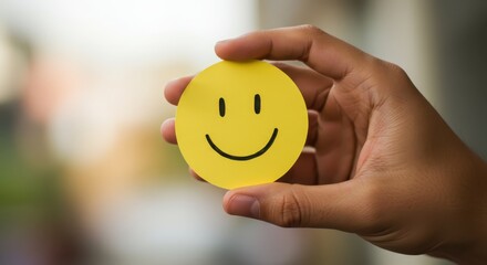 Close up of a hand holding a yellow round piece of paper with a smiley face drawn on it