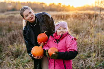 Girl with Down syndrome and mother holding pumpkins in dry grass field
