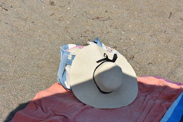 Summer layout with a sun hat and a bag on the beach towels. Vacation, travel and summer concept. Summer beach holidays in Sicily, Italy. Relaxing on the beach. Beach near Cefalu. Travel to Italy. 