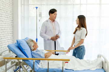 Senior female patient receiving care in hospital room with doctor consulting family member beside...
