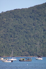 Scenic view of the sea with traditional boats, children playing on the beach, and calm coastal waters in Barra Seca, Ubatuba, Brazil. Authentic tropical life and natural beauty