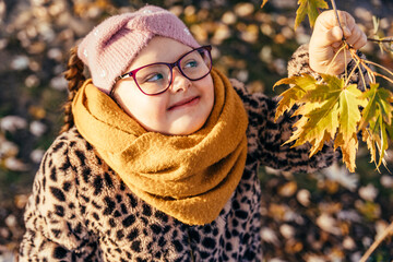 Girl with Down syndrome smiling and reaching for autumn leaves