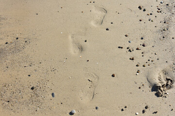 Imprints of human bare feet on the fine sand, on the beach smoothed by low tide. Footprints of human feet. Concept for travel and vacation. Beach near Cefalu, in Sicily, Italy. Travel to Italy. Relax.