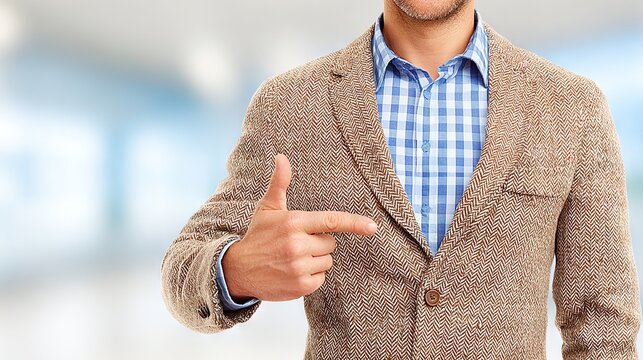 Confident man in a brown blazer and checkered shirt pointing sideways with index finger, highlighting direction or presenting business focus - Powered by Adobe