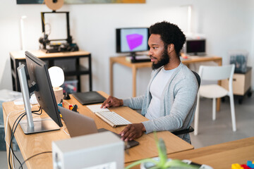 An African American man works diligently at his desk, focused on his computer setup. He uses a keyboard and trackpad in a modern office environment.