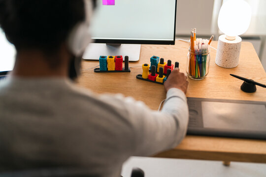 An African American person wearing headphones works at a desk, looking at a computer. They interact with a colorful educational toy, surrounded by office supplies.