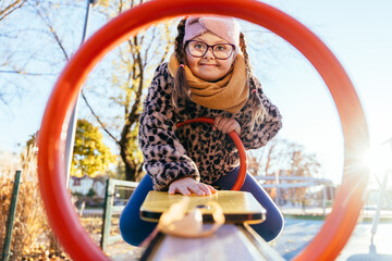 Brave girl with Down syndrome leaning forward on seesaw
