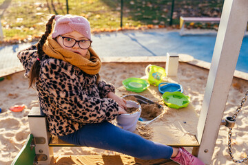 Playful girl with Down syndrome sitting in sandbox with toys