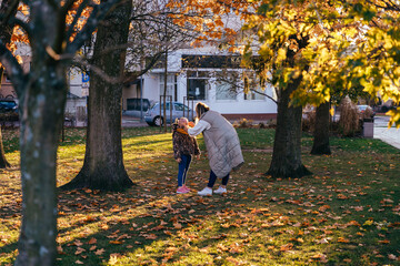 Mother adjusting girl's scarf in autumn park
