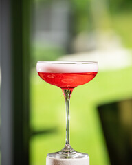 A vibrant pink cocktail with a delicate white foam top is perfectly balanced on a white textured...